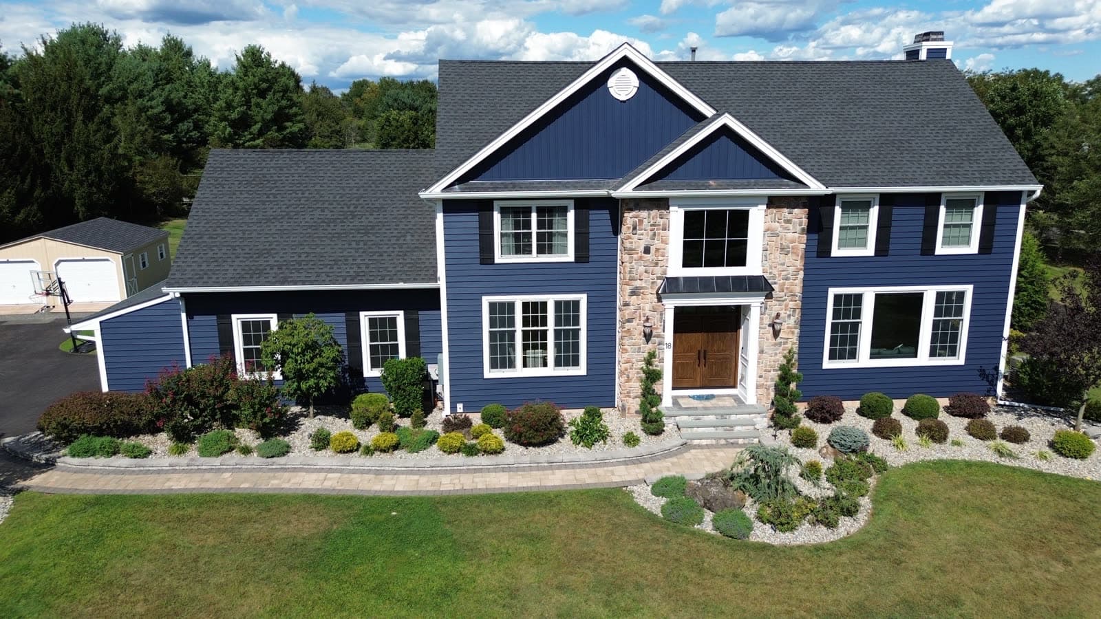 Same New Jersey colonial after Revive renovation — deep navy lap and board-and-batten siding, stone surround, new windows, and a new roof
